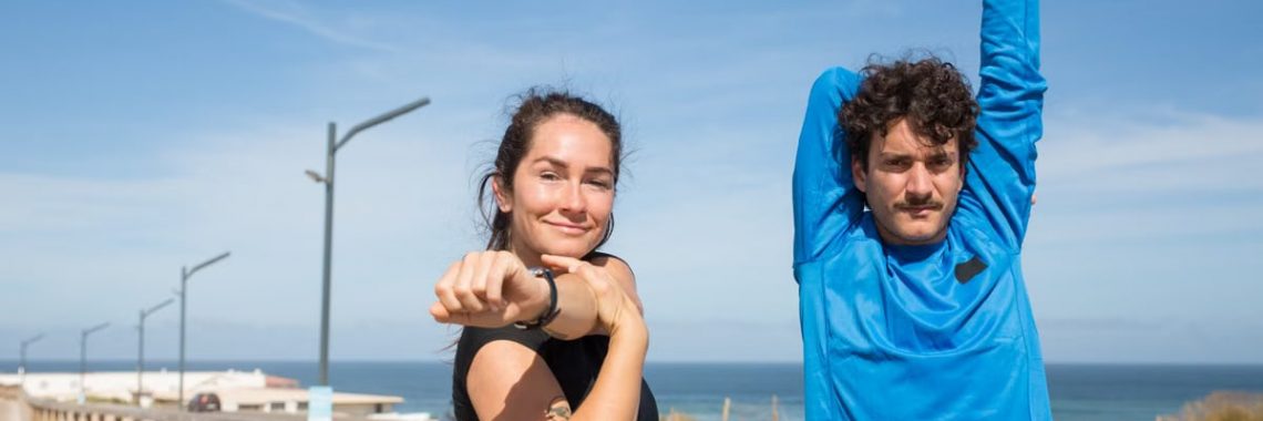 Active young couple stretching outdoors by the ocean on a sunny day in Portugal.